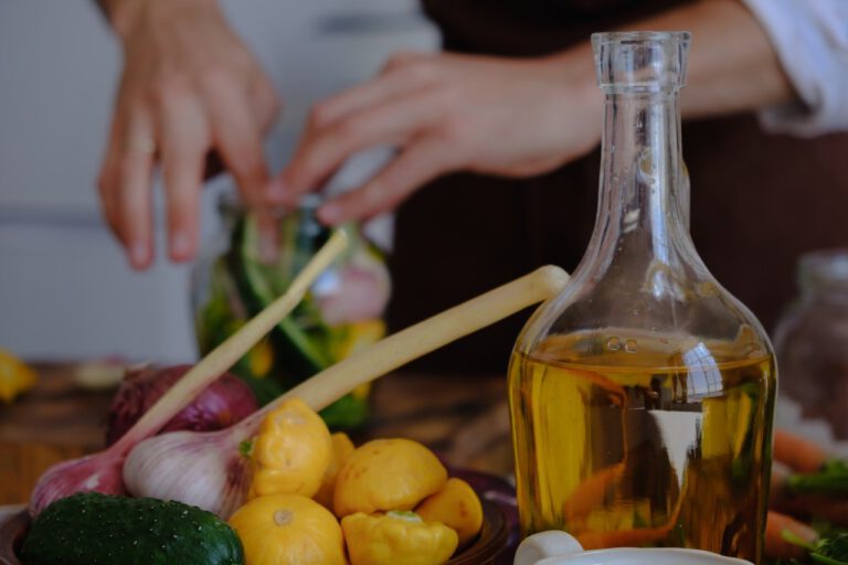 Clear glass bottle filled with cooking oil next to onion and squash