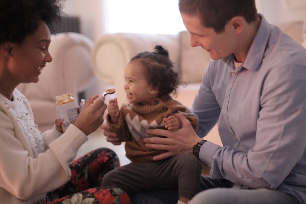 Mom spoon feeding a toddler while the dad holds the child