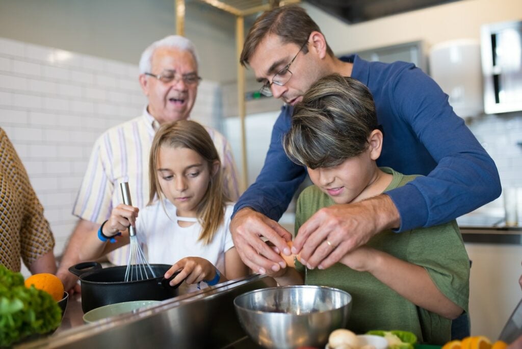 Man in Blue Sweater Assisting the Boy in Green Shirt Cracking Eggs