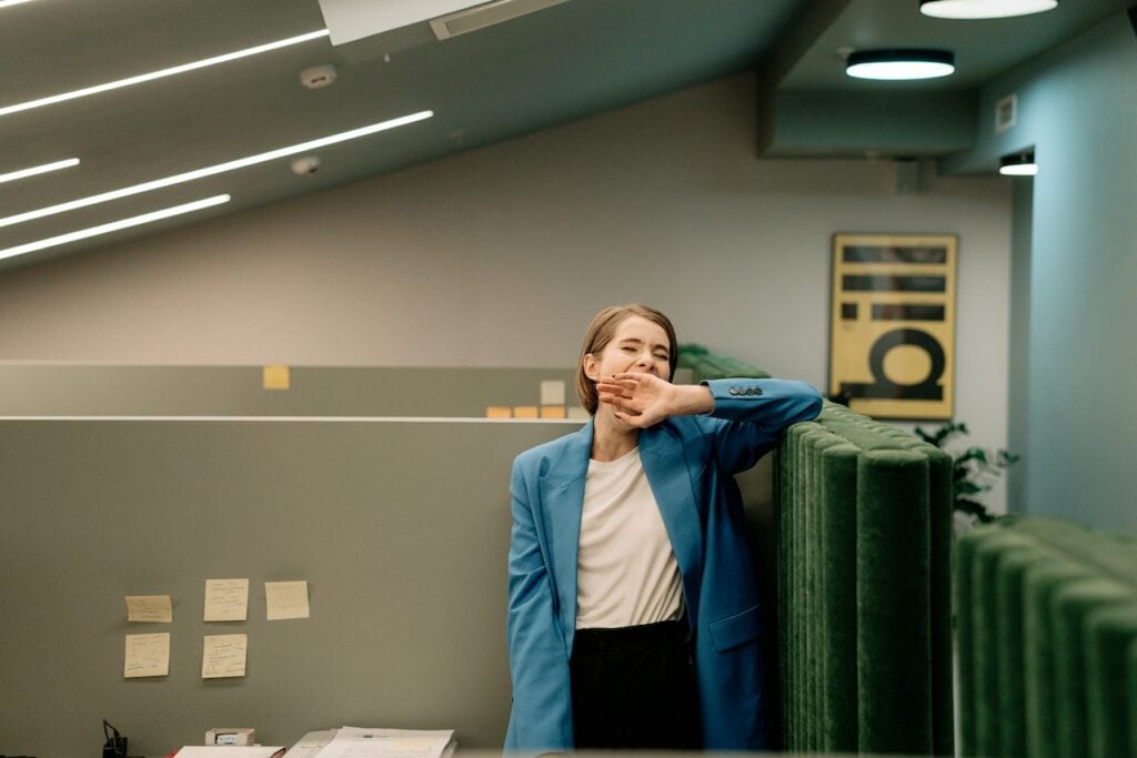 A woman in a blue blazer yawning at the office