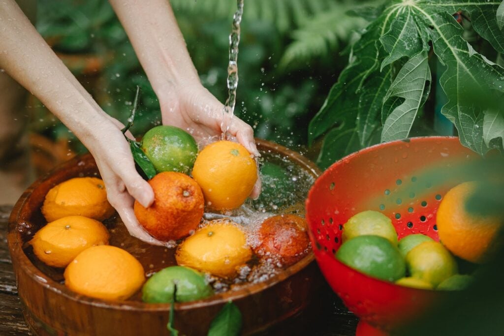 Woman washing citrus fruits in a large brown bowl